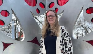 Woman with glasses standing outside in front of a gray and red sculpture