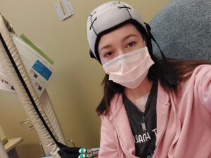 Brunette woman wearing a soft cap and medical face mask sitting in a clinic room