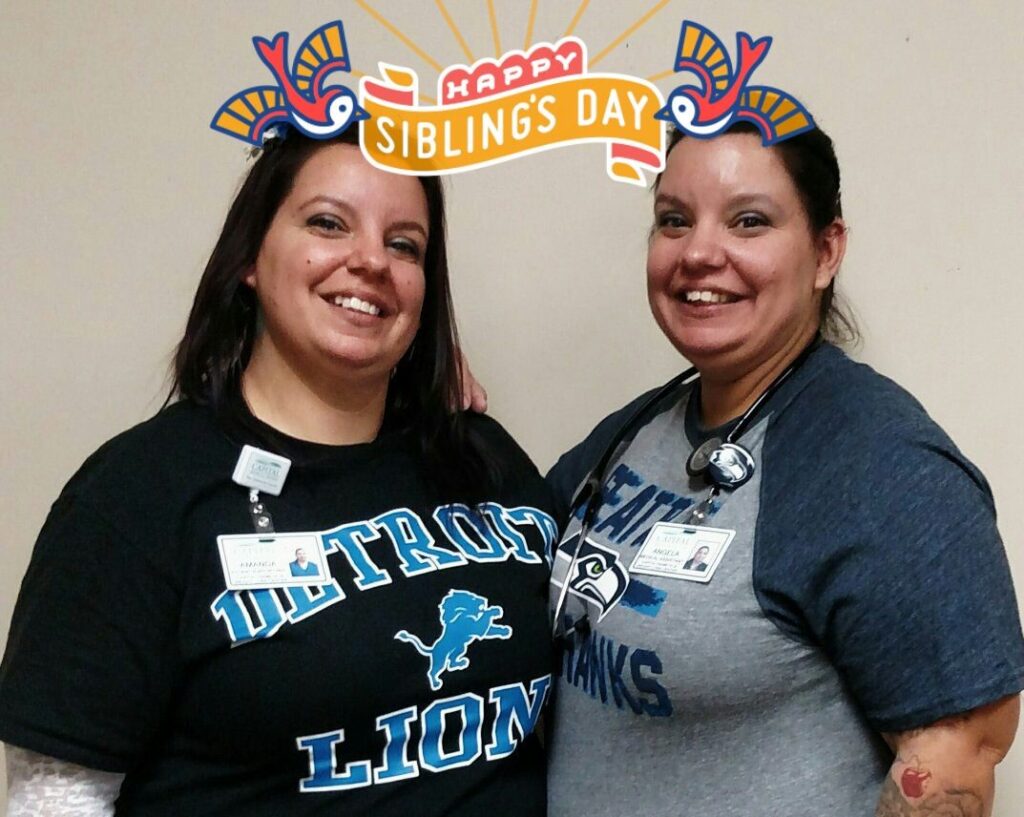 twin women smile for the camera, wearing employee ID badges; twin on left has long dark hair and twin on right has a stethoscope around her neck and dark hair pulled back; text overlay at top reads “Happy Sibling’s Day”