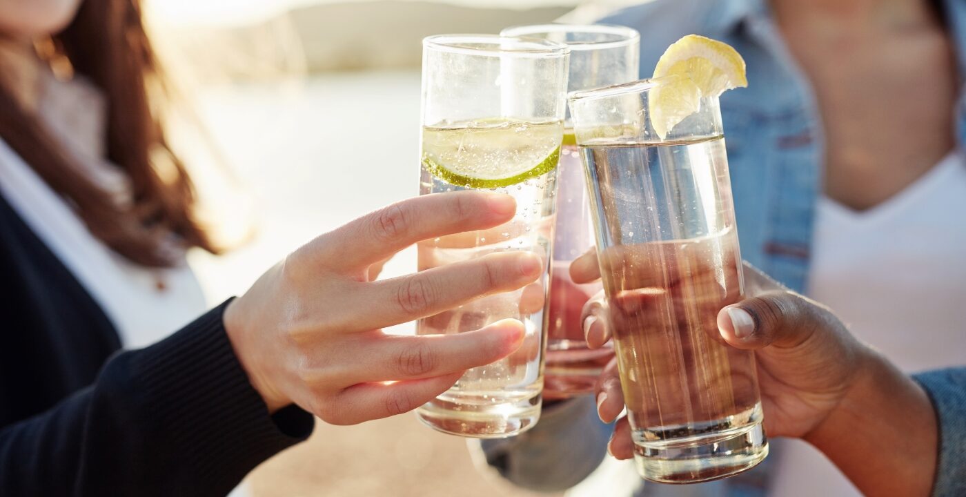 People raising glasses of a clear liquid with lime wedges in a toast