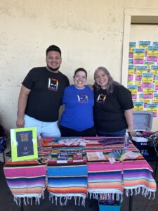 Three people stand at a table with informational materials