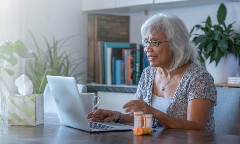 Senior woman sitting in front of a laptop next to medication bottles