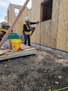 Woman in hard hat and reflective vest examines wall of home under construction