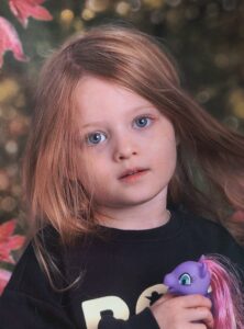 Child with long hair holds a purple toy pony outdoors, with soft-focus foliage and autumn leaves in the background.