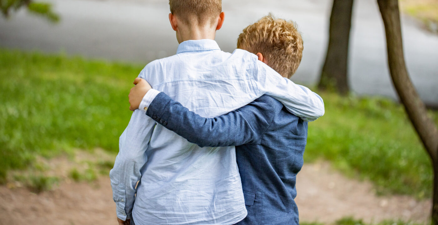 Two young boys shown from back with arms around each other’s shoulders