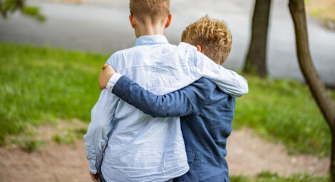 Two young boys shown from back with arms around each other’s shoulders