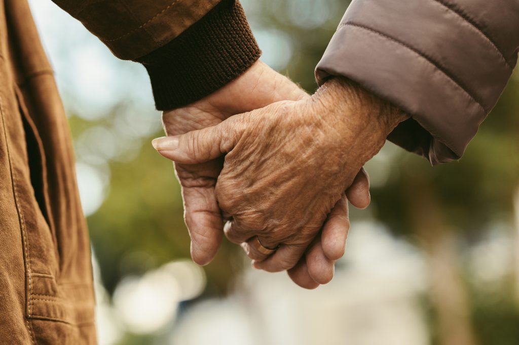 Close up of elderly couple holding hands and walking outdoors.