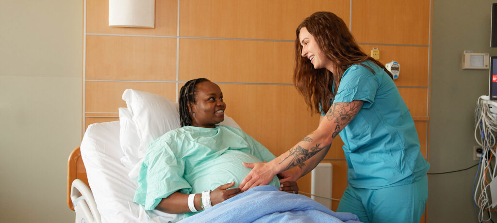 Smiling pregnant woman in hospital bed, being examined by a nurse.