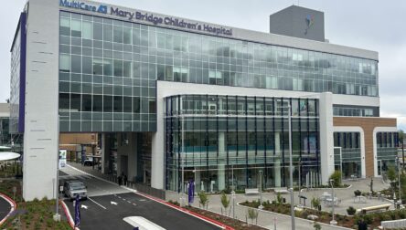 Exterior view of MultiCare Mary Bridge Children’s Hospital, showing a modern glass‑fronted building with the hospital name displayed above the main entrance and a curved driveway in front.