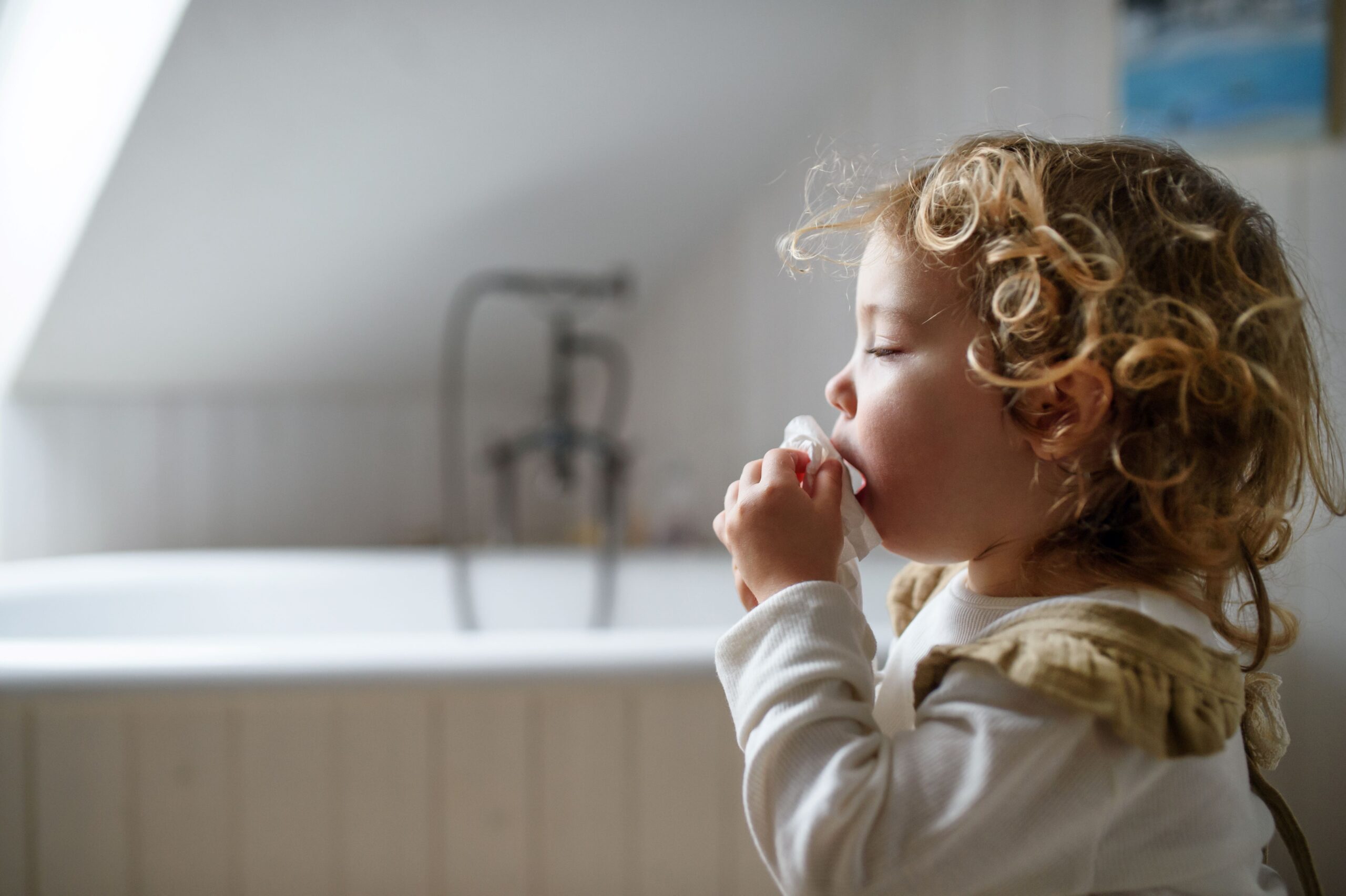 Sick toddler coughing into a tissue