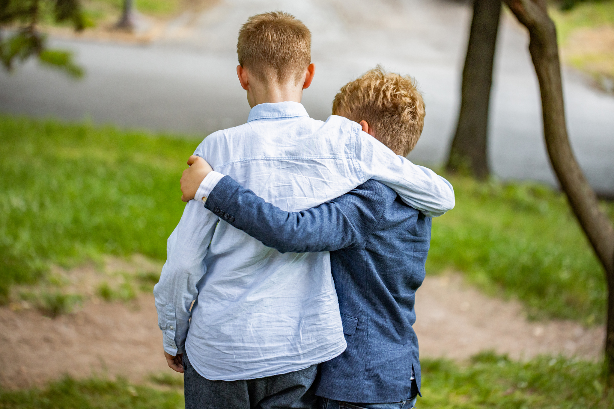 Two young boys shown from back with arms around each other’s shoulders